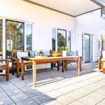 Terrasse mit Holztisch, Stühlen und Sonnenschutz. Hintergrund: Haus mit Fenstern.