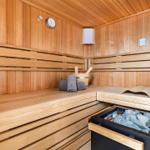 Sauna mit Holzbank, Thermometer und Steinen im Ofen.