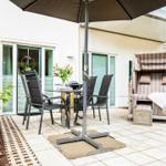 Terrace with table, chairs, umbrella, and beach chair. Background: house with windows.