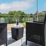 Terrace with two black wicker chairs and table. Glass railing and forest in background.