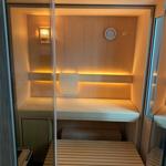 Sauna with wooden bench, thermometer, and warm lighting.