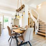 Dining room with table, chairs, and spiral staircase. Ceiling light with wooden pipe and bulbs.