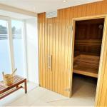 Sauna mit Holzbank und Fensterblick auf Wald. Holzgestell und Tür sind sichtbar.