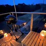 Terrasse mit Grill, Holztisch und Kerzen bei Dämmerung.