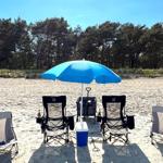 Blauer Strandparasol mit Stühlen und Kühler auf Sandstrand vor Wald.