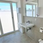 Badezimmer mit Waschbecken, Spiegel und Glastür zum Balkon.
