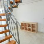 Treppenhaus mit Holzstufen und Metallgeländer, daneben steht ein Holzregal.