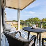 Terrasse mit Sitzgruppe und Tisch. Blick auf Wald und Gebäude.