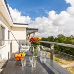 Terrasse mit Tisch, Stühlen, Blumen und Obst. Blick auf Wald und Himmel.