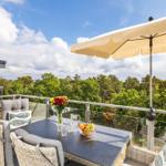 Terrasse mit Tisch, Stühlen und Sonnenschutz. Blick auf Wald und Himmel.
