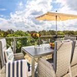 Terrasse mit Tisch, Stühlen und Sonnenschirm. Blick auf Wald und Himmel.