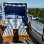 Hochwertiger Strandkorb mit blau-weißem Streifenmuster auf Balkon mit Blick auf Wald und Wasser.