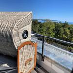 Terrasse mit Rattanliege und Blick auf Wald und Meer.