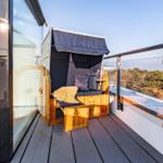 Terrace with wooden lounger, dark blue canopy, and view of forest.