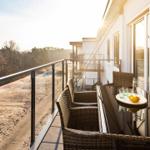 Terrace with table and chairs, view of forest and sandy beach.