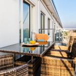 Terrace with table, chairs, and drinks. View of buildings and landscape.