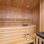 Sauna mit Holzbank, Handtuch und Eimer mit Flaschen.
