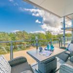 Terrasse mit Sitzgruppe und Tisch, Blick auf Wald und Himmel.