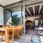 Terrasse mit Holztisch und Stühlen. Durch Glastüren ist Küche und Wohnbereich sichtbar.