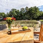 Holztisch mit Weinflaschen und Obst im Freien, Blick auf Wald und Strand.