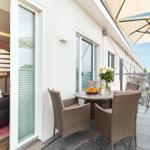 Terrasse mit Tisch, Stühlen und Sonnenschutz. Blick auf Wohnbereich mit Sofa und Treppe.