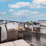 Terrasse mit Sitzgelegenheiten, Tisch und Pflanze unter blauem Himmel mit Wolken.