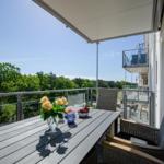 Terrace with table, chairs, and view of green trees under clear sky.