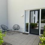 Terrace with two chairs and table in front of glass door. Surrounded by plants and light walls.