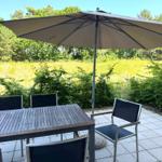 Terrace with table, chairs, and umbrella. Background: meadow and trees.