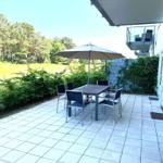 Terrace with table, chairs, and umbrella. Background: green field and trees.
