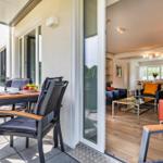 Terrace with table and chairs. Through glass doors, living room with sofa and couch is visible.