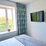 Bedroom with view of greenery, TV mounted on wall, bed with gray cover, sailboat-patterned curtains.