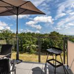 Terrace with umbrella, grill, and view of forest and sea.