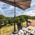 Terrace with table, chairs, and umbrella. View of forest and sea.