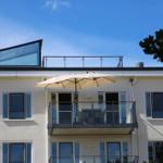 Fassade mit Balkon, Sonnenschirm und Glasgeländer unter blauem Himmel.