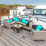 Terrasse mit Sofa, Sitzgruppe und Tisch. Blick auf Wald und Gebäude.