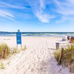 Sandweg führt zum Strand mit Strandkörben und Meer im Hintergrund.