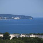 Blick auf das Meer und eine bewaldete Küstenlinie mit Gebäuden.