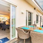 Terrasse mit Esstisch und Stühlen. Durch Glastür ist Wohn- und Essbereich sichtbar.