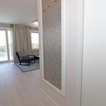Ein Raum mit Holzboden, einem Sessel und großen Fenstern mit Blick auf die Außenterrasse.
