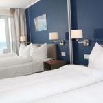 Zimmer mit zwei Betten, blauer Wand und Meerblick durch Fenster.