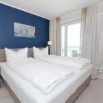 Schlafzimmer mit Doppelbett, blauer Wand und Meerblick durch Fenster.