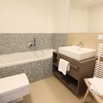 Badezimmer mit Badewanne, Waschbecken und Toilette. Mosaikfliesen an der Wand.