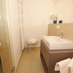 Badezimmer mit Waschbecken, Spiegel und Sauna. Holzstuhl und Handtücher.