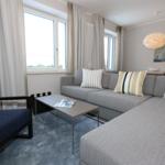 Wohnzimmer mit Sofa, Sessel, Couchtisch und Fenstern mit Vorhängen.