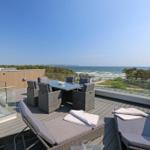 Terrasse mit Sitzgruppe und Meerblick. Holzdeck und Glasgeländer.