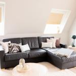 Schwarzes Ledersofa mit Kissen und Decke, runder Tisch, Fenster mit Jalousien.