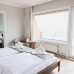 Schlafzimmer mit Doppelbett, Sitzgelegenheit und Blick auf Balkon.