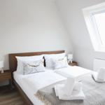 Schlafzimmer mit Dachschrägen, Bett mit Kissen, Nachttisch und Fenster.