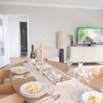 Gesetzter Tisch mit Tellern und Gläsern. Fernseher und Sessel im Hintergrund.
